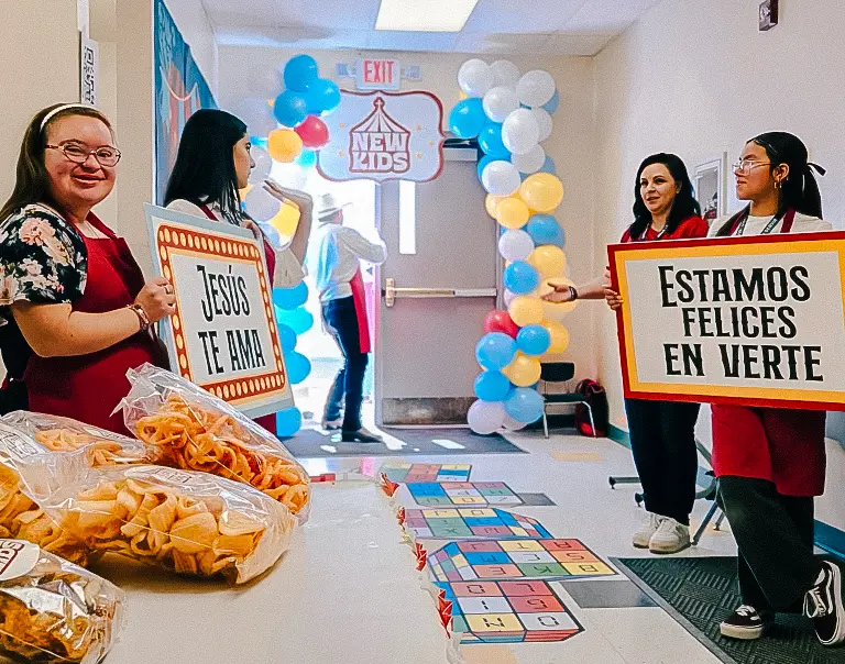 Voluntarias en entrada de área infantil con letreros de bienvenida y botanas.